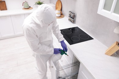 Photo of Pest control worker in protective suit spraying insecticide at home, above view