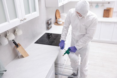 Photo of Pest control worker in protective suit spraying insecticide at home