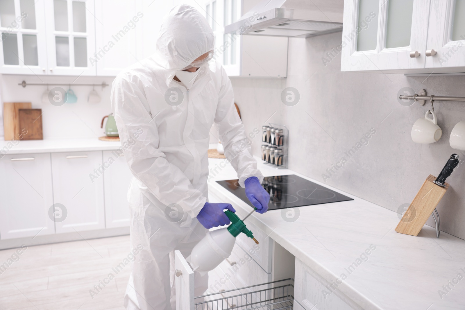 Photo of Pest control worker in protective suit spraying insecticide at home