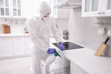 Photo of Pest control worker in protective suit spraying insecticide at home