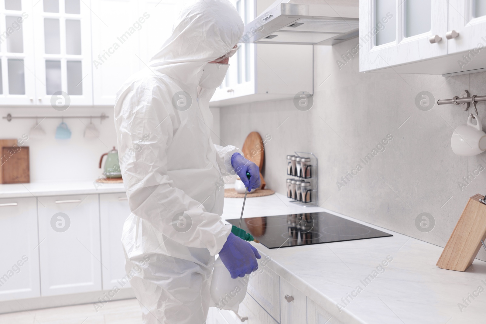 Photo of Pest control worker in protective suit spraying insecticide at home