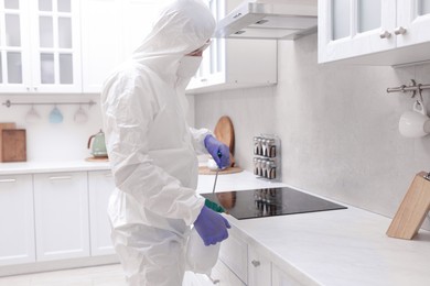 Photo of Pest control worker in protective suit spraying insecticide at home