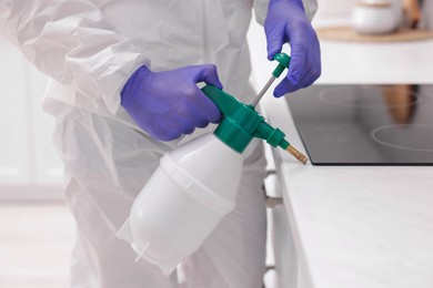 Photo of Pest control worker in protective suit spraying insecticide at home, closeup