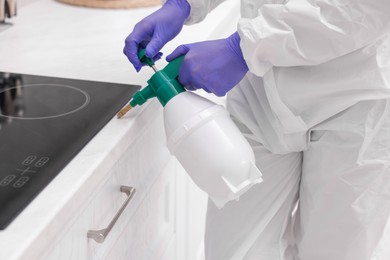 Photo of Pest control worker in protective suit spraying insecticide at home, closeup
