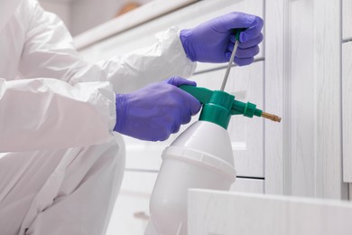 Photo of Pest control worker in protective suit spraying insecticide at home, closeup
