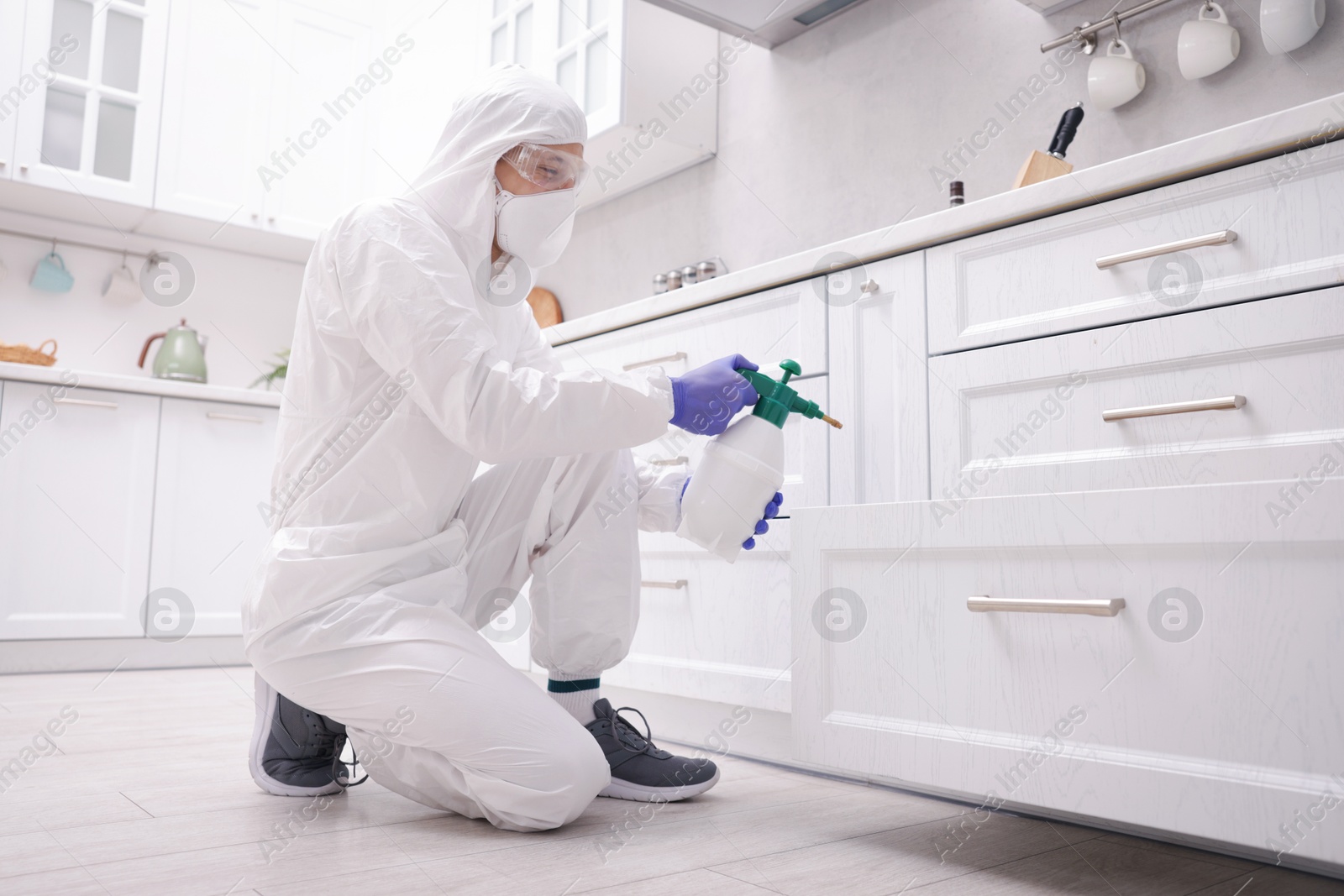Photo of Pest control worker in protective suit spraying insecticide at home, low angle view