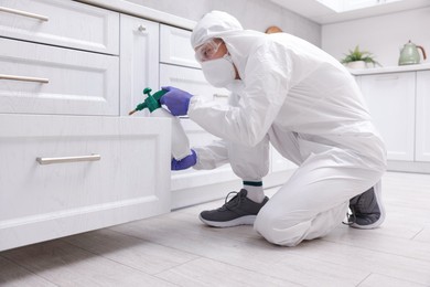 Photo of Pest control worker in protective suit spraying insecticide at home