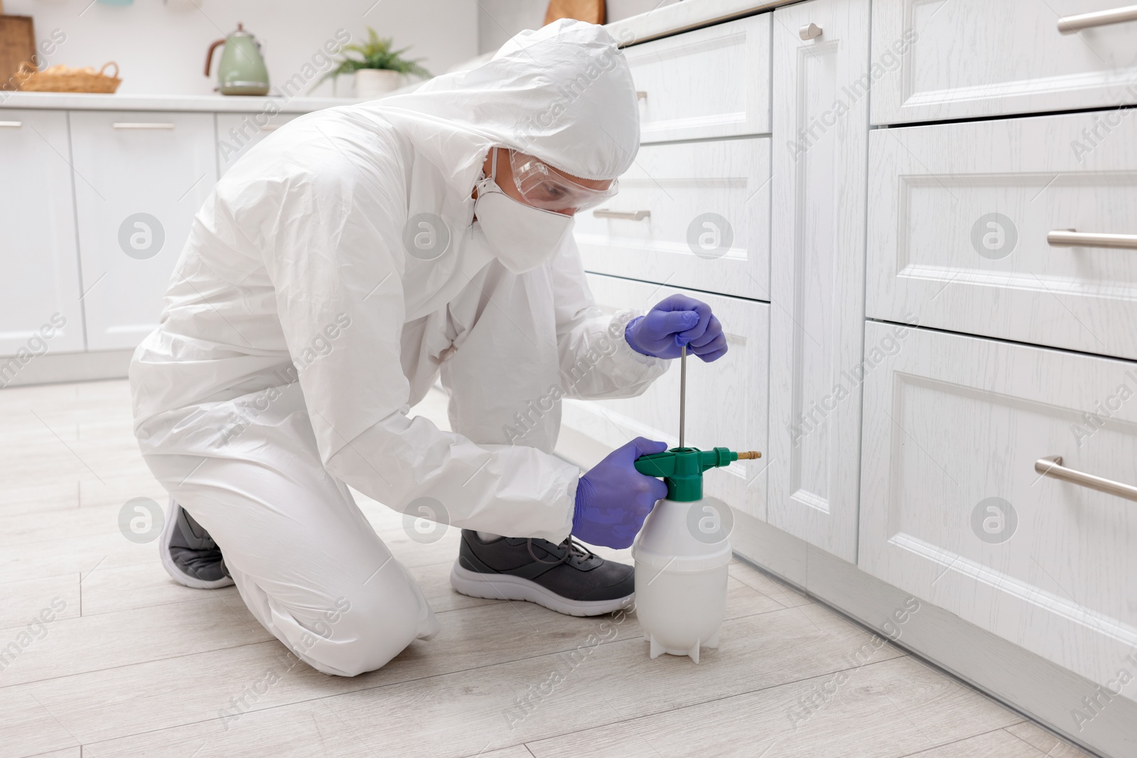 Photo of Pest control worker in protective suit spraying insecticide at home