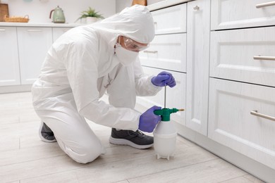 Photo of Pest control worker in protective suit spraying insecticide at home