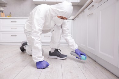 Photo of Pest control worker in protective suit spraying insecticide at home