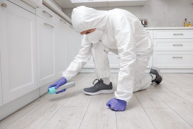 Photo of Pest control worker in protective suit spraying insecticide at home