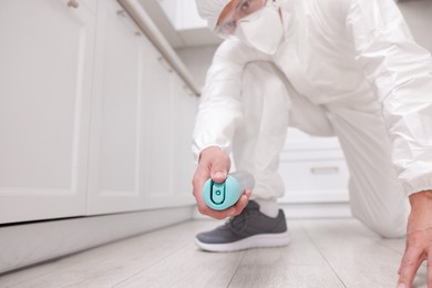Photo of Pest control worker in protective suit spraying insecticide at home, closeup
