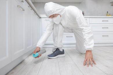 Photo of Pest control worker in protective suit spraying insecticide at home
