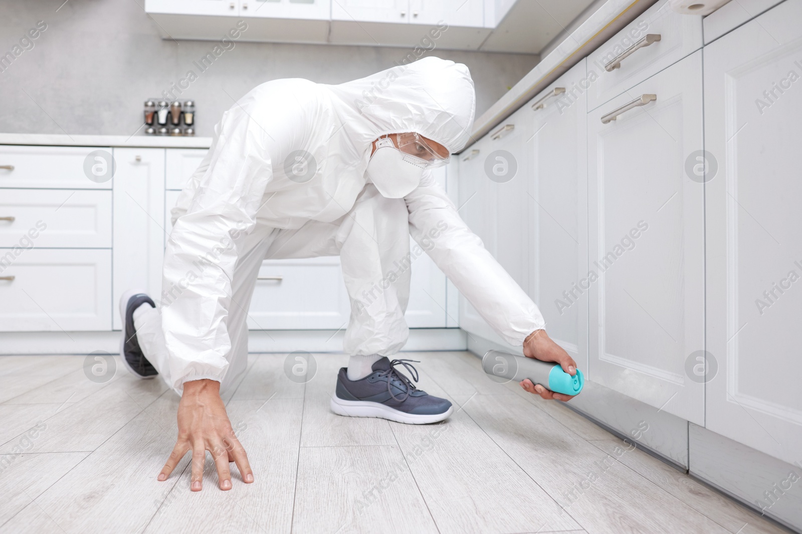 Photo of Pest control worker in protective suit spraying insecticide at home