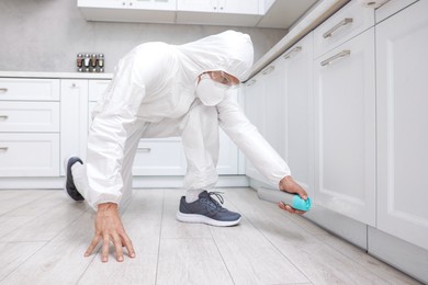 Photo of Pest control worker in protective suit spraying insecticide at home
