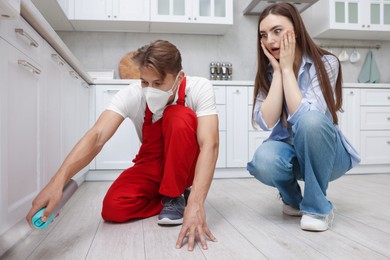 Photo of Worried woman and pest control worker spraying insecticide at home