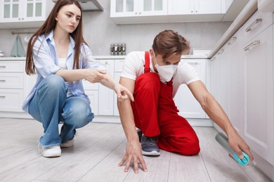 Photo of Worried woman and pest control worker spraying insecticide at home