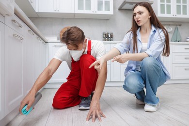 Photo of Worried woman and pest control worker spraying insecticide at home