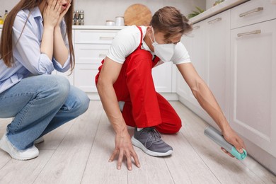 Photo of Worried woman and pest control worker spraying insecticide at home
