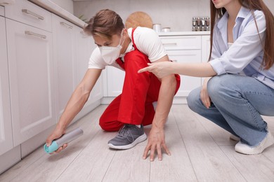 Photo of Worried woman and pest control worker spraying insecticide at home