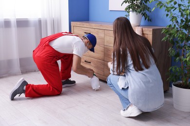 Photo of Worried woman and pest control worker spraying insecticide at home