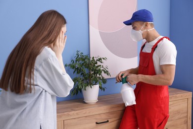 Photo of Worried woman and pest control worker spraying insecticide at home