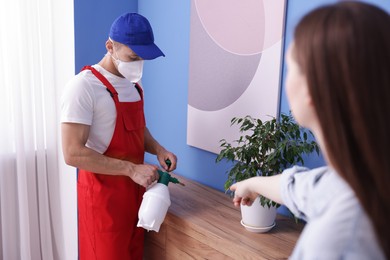 Photo of Worried woman and pest control worker spraying insecticide at home
