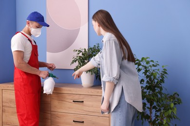 Photo of Worried woman and pest control worker spraying insecticide at home