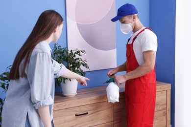 Photo of Worried woman and pest control worker spraying insecticide at home