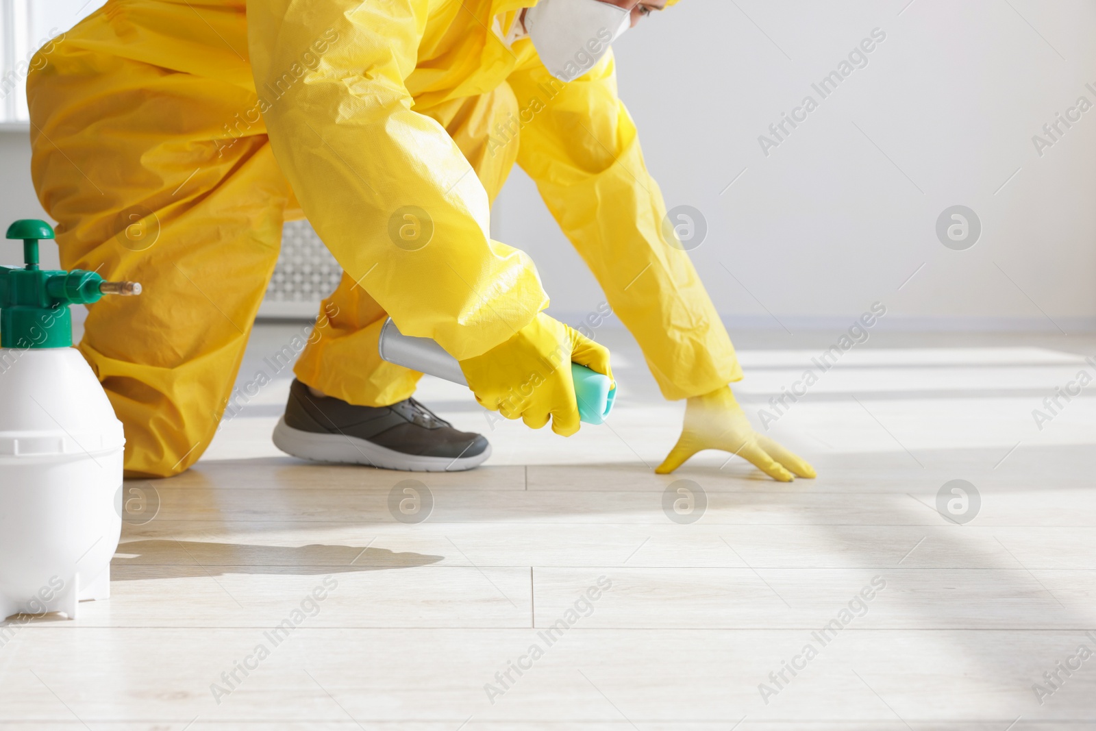 Photo of Pest control worker in protective suit spraying insecticide indoors, closeup
