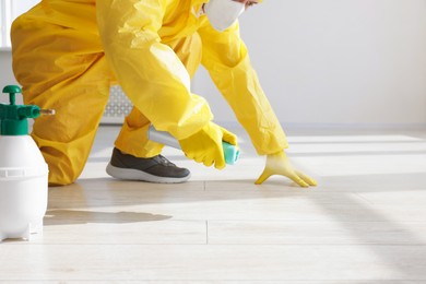 Photo of Pest control worker in protective suit spraying insecticide indoors, closeup