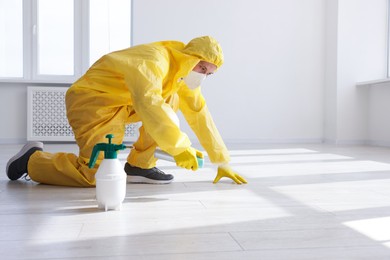 Photo of Pest control worker in protective suit spraying insecticide indoors. Space for text