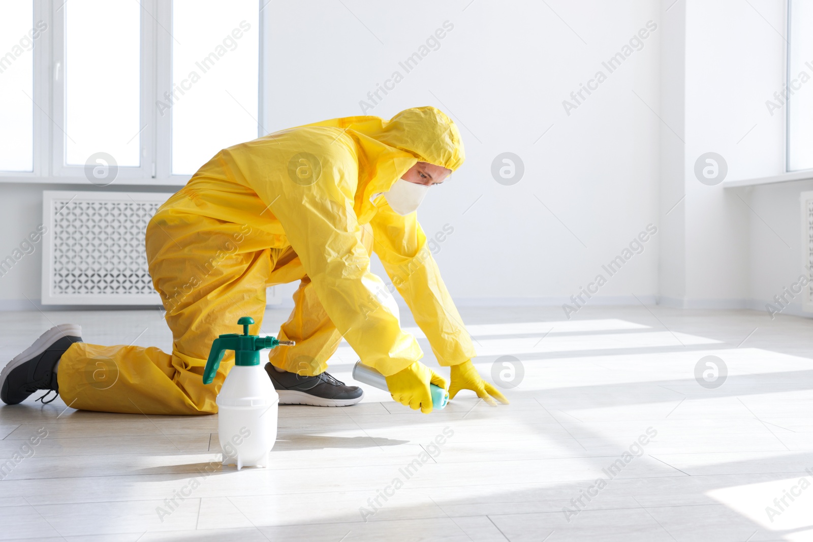 Photo of Pest control worker in protective suit spraying insecticide indoors. Space for text