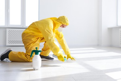 Photo of Pest control worker in protective suit spraying insecticide indoors. Space for text