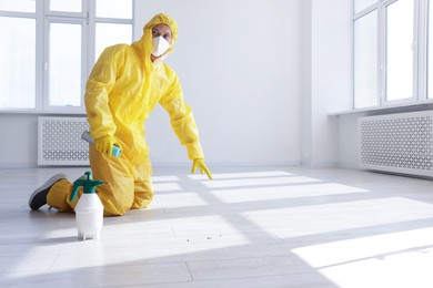 Photo of Pest control worker in protective suit spraying insecticide indoors. Space for text