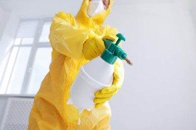 Photo of Pest control worker in protective suit spraying insecticide indoors, closeup