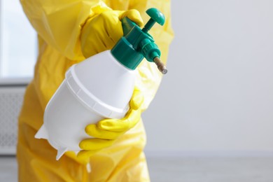 Photo of Pest control worker in protective suit spraying insecticide indoors, closeup