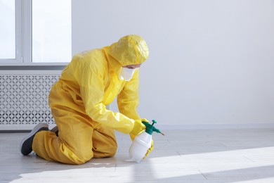 Photo of Pest control worker in protective suit spraying insecticide indoors. Space for text