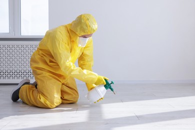 Photo of Pest control worker in protective suit spraying insecticide indoors. Space for text