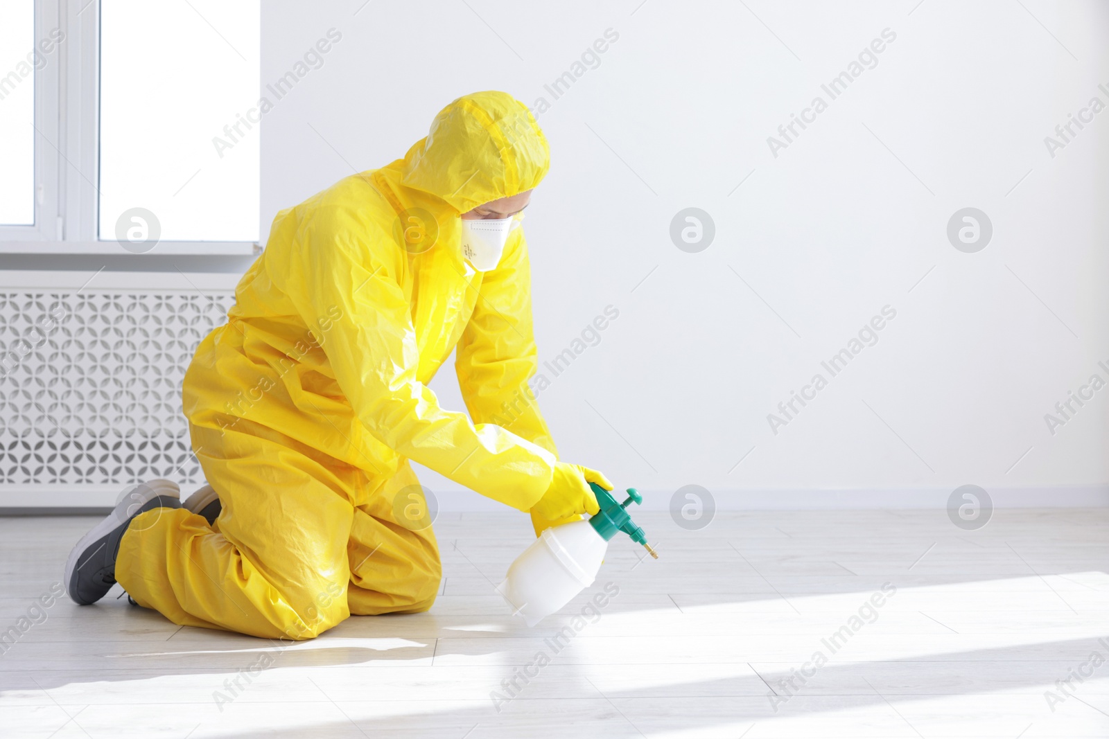 Photo of Pest control worker in protective suit spraying insecticide indoors. Space for text
