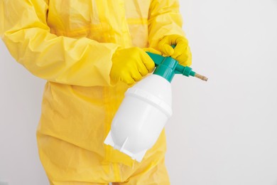 Photo of Pest control worker in protective suit spraying insecticide near white wall, closeup