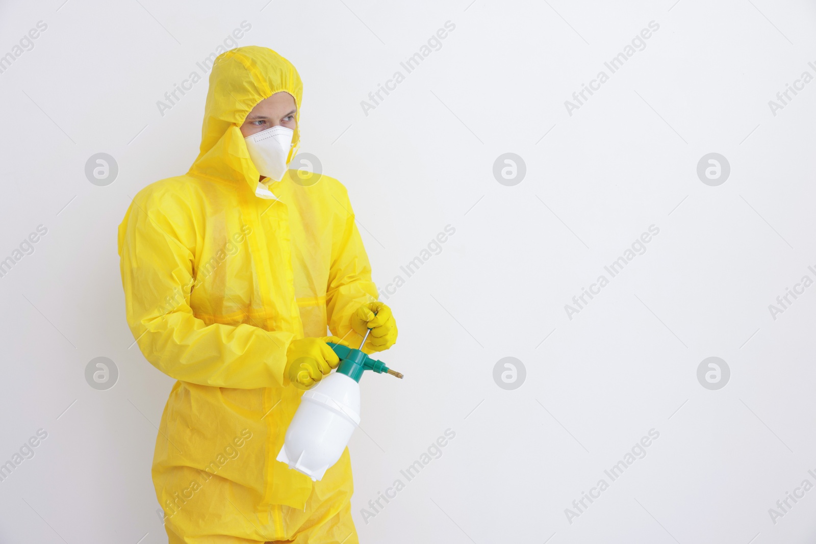 Photo of Pest control worker in protective suit spraying insecticide near white wall. Space for text