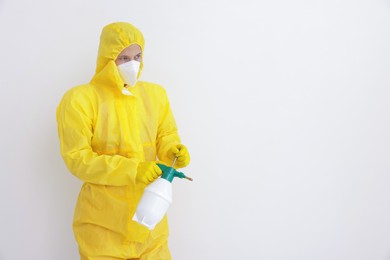 Photo of Pest control worker in protective suit spraying insecticide near white wall. Space for text