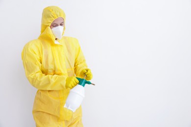 Photo of Pest control worker in protective suit spraying insecticide near white wall. Space for text