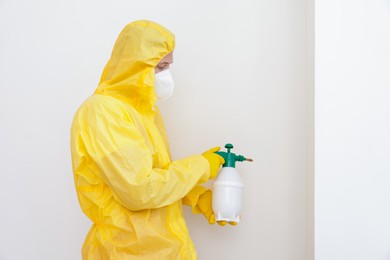 Photo of Pest control worker in protective suit spraying insecticide near white wall. Space for text