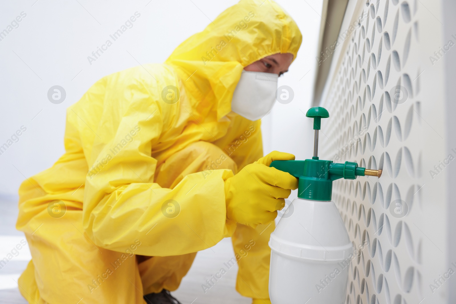 Photo of Pest control worker in protective suit spraying insecticide indoors, selective focus