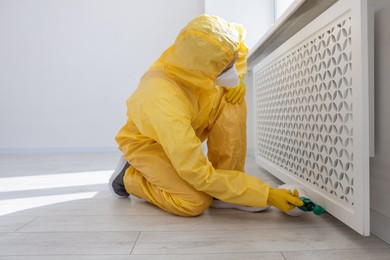 Photo of Pest control worker in protective suit spraying insecticide indoors