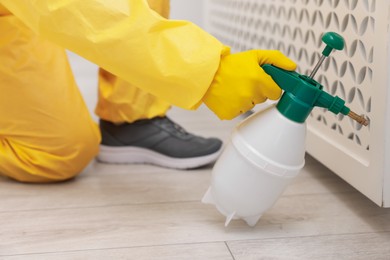 Photo of Pest control worker in protective suit spraying insecticide indoors, closeup