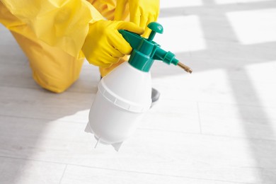 Photo of Pest control worker in protective suit spraying insecticide indoors, closeup