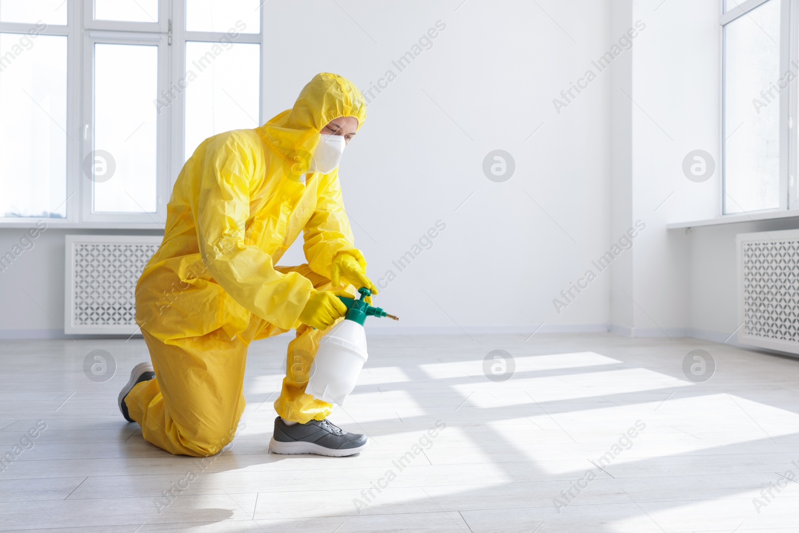 Photo of Pest control worker in protective suit spraying insecticide indoors. Space for text